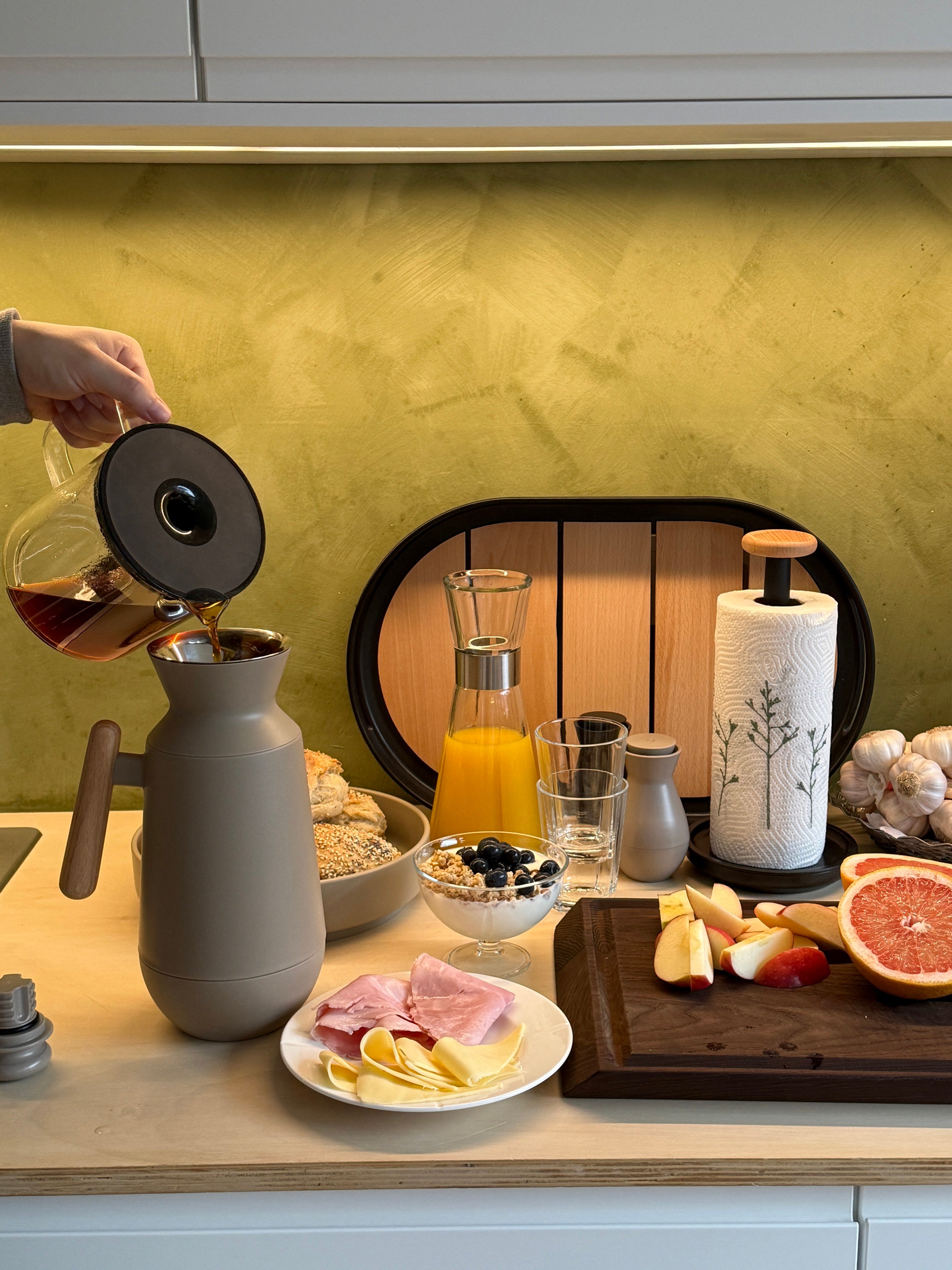 Morgenbord med rundstykker og Rosendahl, hvor der hældes kaffe i en rolig, enkel stemning